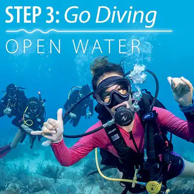 A scuba diver in a pink wetsuit giving thumbs up underwater.