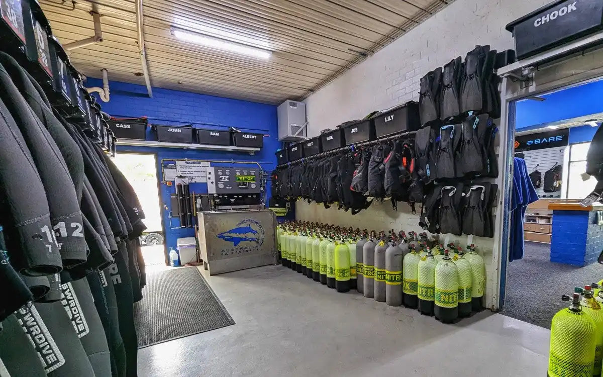 Scuba diving equipment room with wetsuits and air tanks lined up along the walls.