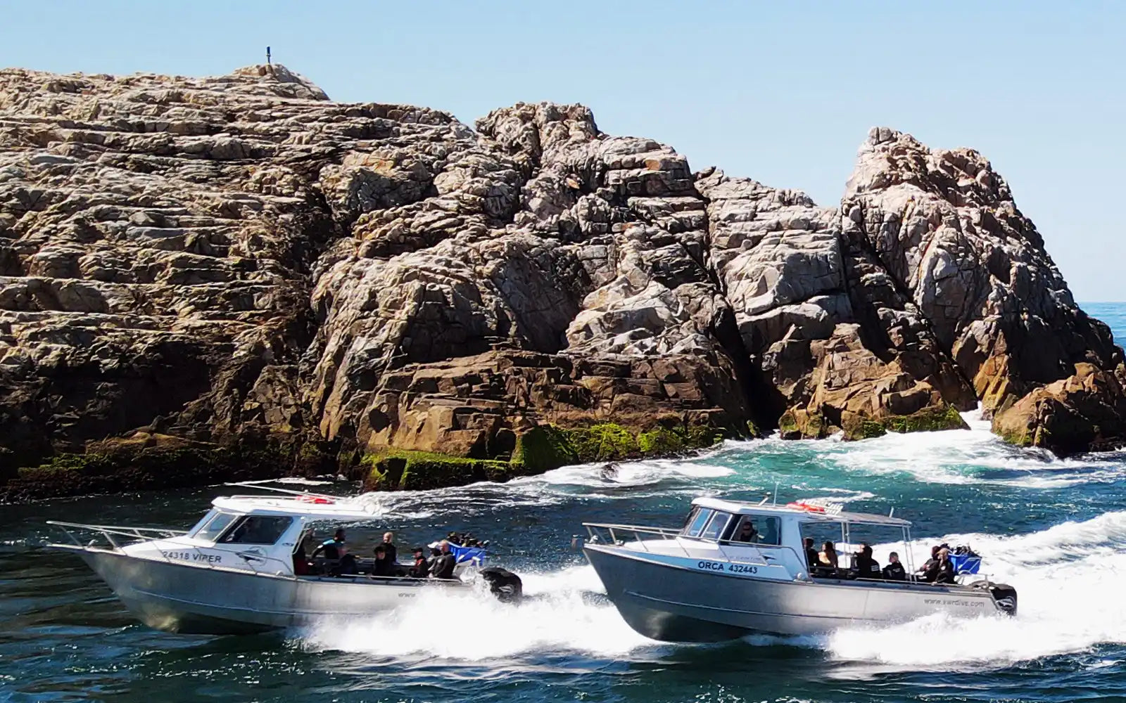 Three motorboats speeding across choppy waters near rocky cliffs.