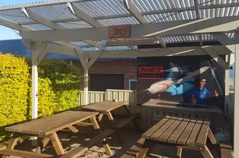 Wooden picnic shelter with slatted roof panels and bench seating.